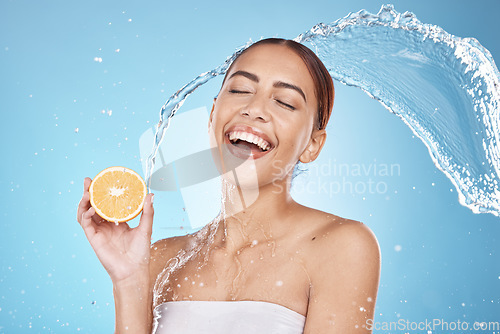 Image of Water splash, orange fruit and skincare happiness in blue studio background for organic facial care cleaning, dermatology detox and spa nutrition. Model face, smile and vitamin c and citrus cosmetics