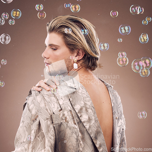 Image of Beauty, lgbtq fashion and man with bubbles in studio on brown background for cosmetics, style and modern outfit. Creative art, luxury design and non binary model with soap bubbles, jewelry and makeup