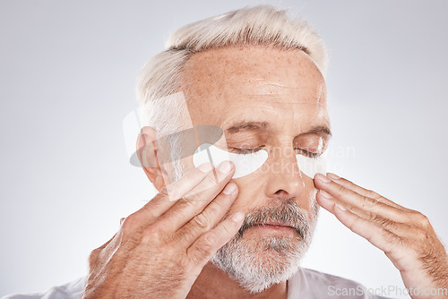 Image of Eyes patch, senior man and skincare face in studio for self care dermatology, facial and cosmetics advertising in morning. Model with hands application of collagen mask or anti aging beauty product