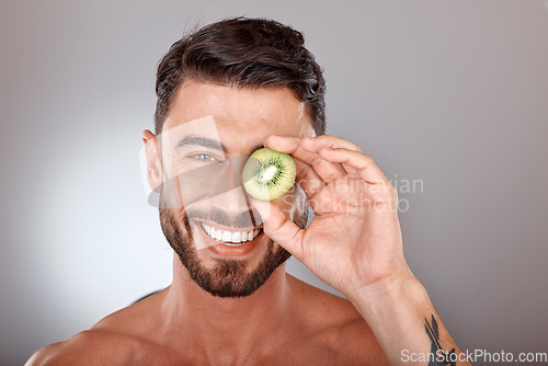 Image of Man, face and beauty with kiwi, facial care with wellness and organic treatment against studio background. Natural skincare, fruit and eye, wellness mockup with cosmetic care and smile in portrait