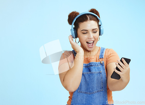 Image of Mockup, smartphone and woman with headphones, excited and smile on blue studio background. Happy, female or girl with cellphone, headset or steaming music, social media or podcast to relax or listen