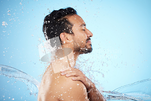 Image of Man, water splash and clean for skincare, wellness and health with beauty, grooming and on blue studio background. Cleaning, male and shower for washing, organic care and hygiene for natural skin.