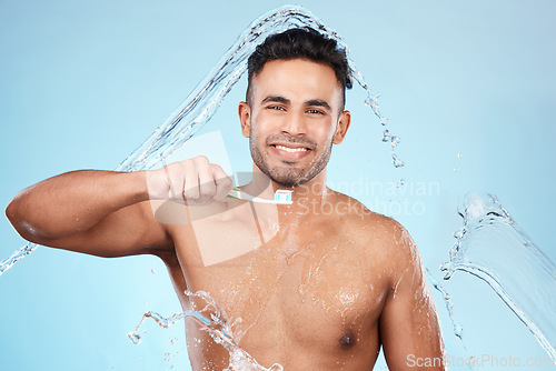 Image of Face, water splash and man with toothbrush for cleaning in studio on blue background. Dental veneers, hygiene and portrait of happy male model brushing teeth for oral wellness, health or fresh breath