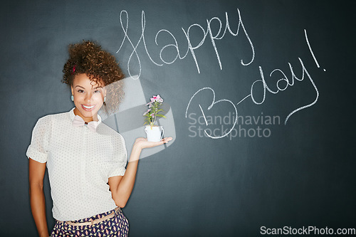 Image of Black woman, studio portrait and holding plant with smile, beauty and celebration of birthday. Woman, teacher and writing wall for happy birthday, b-day and happiness with flowers for gift of growth