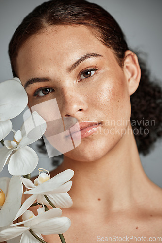 Image of Face portrait, skincare and woman with orchid in studio isolated on a gray background. Floral makeup, organic cosmetics and female model with flowers for healthy skin treatment, wellness and beauty