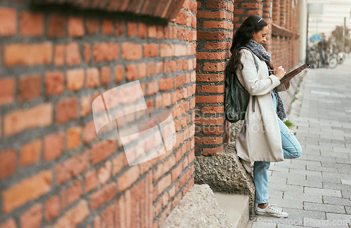 Image of Woman, student and tablet leaning on brick wall writing, design or doing research in the city. Female university learner or designer working on touchscreen with wireless pen or tech in a urban town