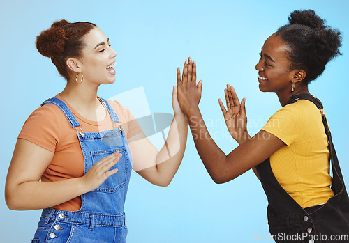 Image of Interracial woman, friends and smile for high five, game or playing and standing isolated on a blue background. Happy women smiling and enjoying playful time together with hands for friendship
