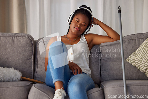 Image of Black woman, sleeping and listening to music on sofa in the living room after housekeeping, cleaning or dusting at home. African American female domestic relaxing or resting with headphones on couch