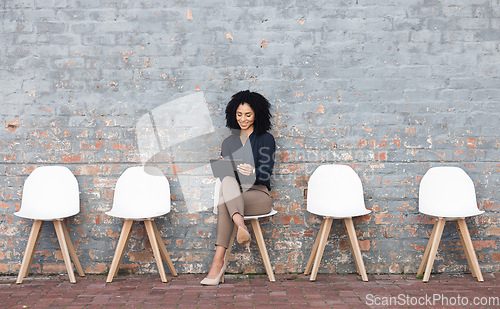 Image of Job search, tablet and black woman in waiting room on brick wall for career opportunity, hr website and internship. Happy person in chair reading hiring email, Human Resources application and faq