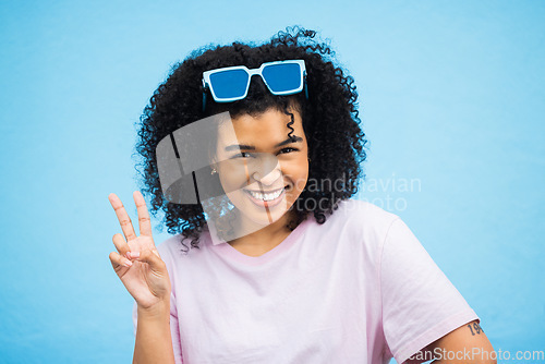 Image of Portrait, black woman and sign for peace, fashion and casual outfit with girl on blue studio background. African American female, confident lady or gesture with sunglasses, happiness and on backdrop