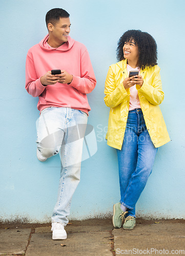 Image of Happy friends, phone and smile leaning on a wall enjoying social media, conversation or communication in the outdoors. Man and woman smiling for networking, 5G connection or chat on mobile smartphone
