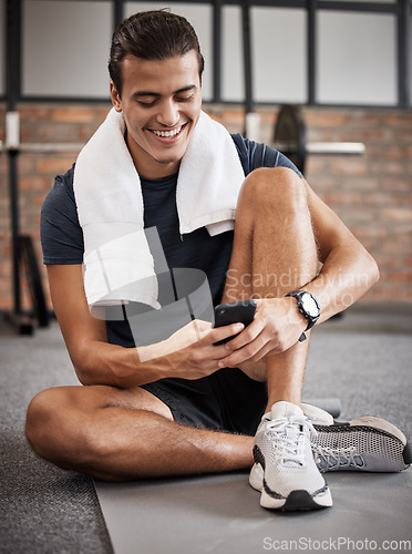 Image of Fitness, man and phone with smile for social media, conversations or chatting while sitting on a mat at gym. Happy sporty male, person or guy smiling in happiness on smartphone after intense workout