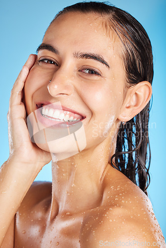 Image of Face portrait, skincare shower and woman in studio isolated on a blue background. Water splash, beauty and happy female feeling fresh after bathing, cleaning and washing for healthy skin and wellness