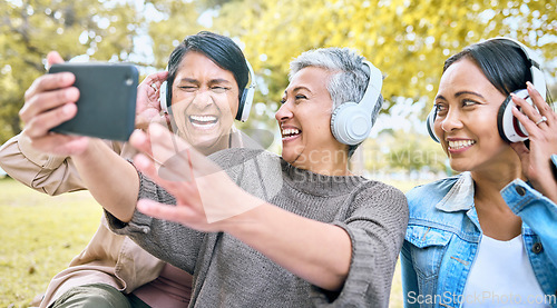 Image of Senior woman, friends and phone laughing with headphones listening to music or watching comedy movie in the park. Group of happy elderly women enjoying funny series or 5G connection on smartphone