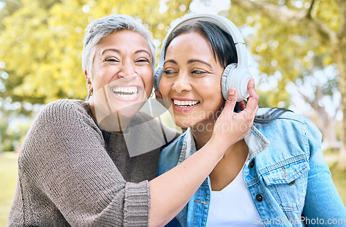 Image of Music, happy and portrait of women in a park streaming a funny podcast, audio and song in India. Laughing, smile and senior friends with headphones listening to a comic sound or radio in nature