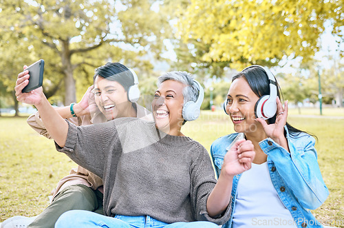 Image of Headphones, friends phone selfie and women at park taking pictures for social media. Mobile, retirement and group of senior females streaming music, taking photo and laughing at comic meme or joke.