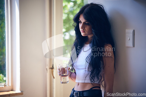 Image of Mental health, depression and sad woman thinking with water, stress and anxiety in a house. Depressed, lonely and goth girl with a drink, emotional and comtemplating problems in the lounge of home