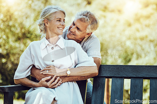 Image of Love, nature and husband hugging his wife from behind while sitting on an outdoor bench in the park. Happy, care and elderly couple embracing on a romantic date together in a green garden in Canada.