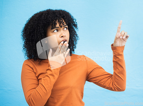 Image of Black woman, surprise face and pointing in studio for news, announcement or gossip notification by blue background. Gen z girl, young african model and fashion with wow hand sign for hearing secret
