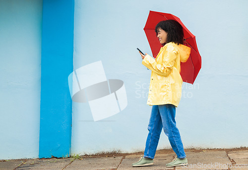 Image of Woman, raincoat and phone typing with umbrella on city street for social media, internet or urban communication. Smile, happy and walking student with mobile technology for weather app check for rain