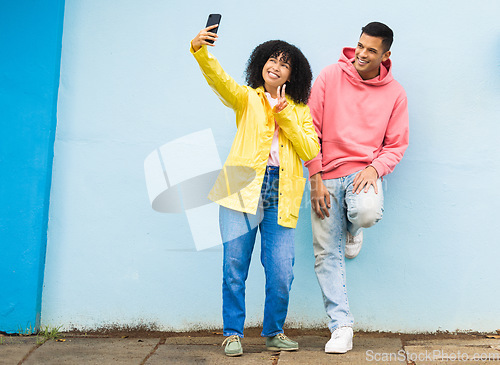 Image of Happy couple, peace sign or phone selfie on isolated blue background for social media, profile picture and travel vlog. Smile, man and black woman bonding for on mobile photography technology in city