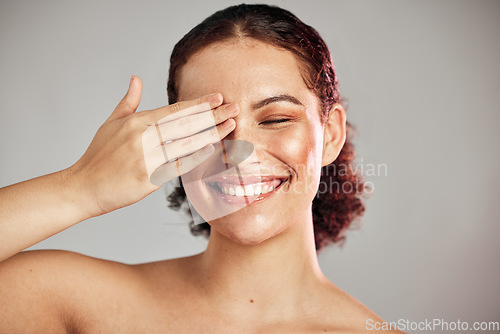 Image of Hand, beauty and woman in studio for makeup, self care and cosmetics, happy and smile on isolated grey background. Face skincare and girl model cover eye for wellness and skin routine while laughing