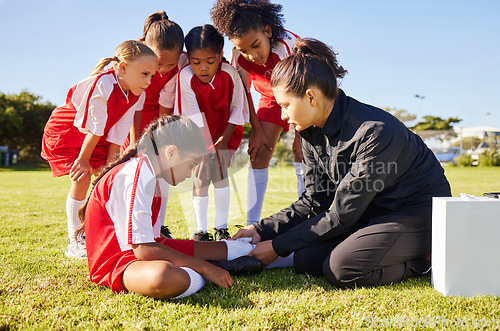 Image of Sports, injury and children soccer team with their coach in a huddle helping a girl athlete. Fitness, training and kid with a sore, pain or muscle sprain after a match on an outdoor football field.