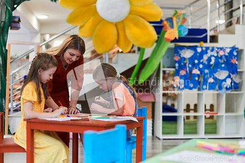 Image of Creative kids during an art class in a daycare center or elementary school classroom drawing with female teacher.