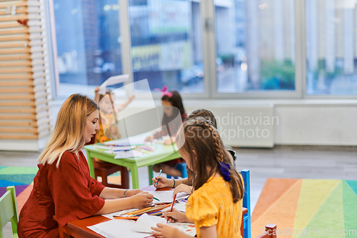 Image of Creative kids during an art class in a daycare center or elementary school classroom drawing with female teacher.