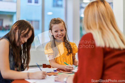 Image of Creative kids during an art class in a daycare center or elementary school classroom drawing with female teacher.