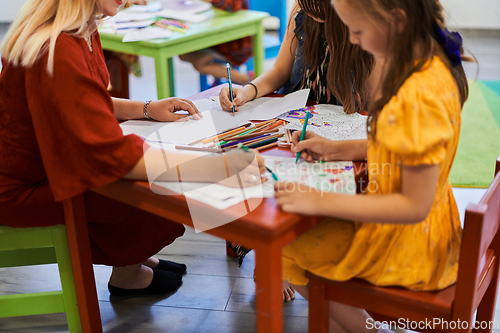 Image of Creative kids during an art class in a daycare center or elementary school classroom drawing with female teacher.