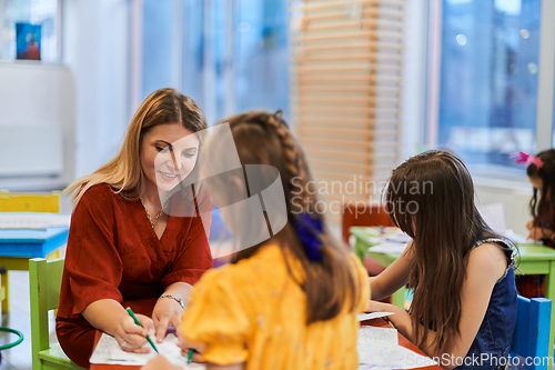 Image of Creative kids during an art class in a daycare center or elementary school classroom drawing with female teacher.