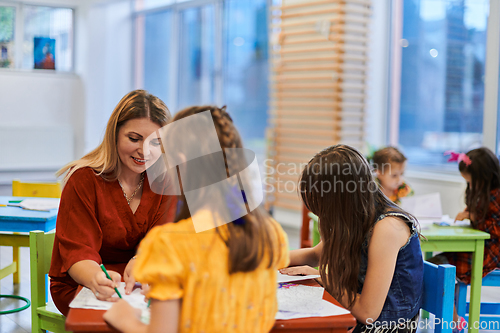 Image of Creative kids during an art class in a daycare center or elementary school classroom drawing with female teacher.