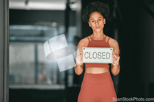 Image of Fitness, portrait or personal trainer at gym with a closed sign for workout exercises or training. Manager, bankruptcy or serious black woman holding a board to stop exercising in empty health club