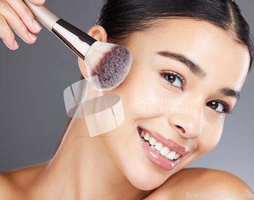 Image of Face, beauty makeup and woman with brush in studio isolated on a gray background. Portrait, aesthetics and happy young female model apply powder, foundation or cosmetics product for skincare wellness