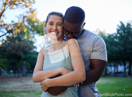 Image of Happy interracial couple, hug and smile for love, care or bonding together in the nature park. Woman smiling with man hugging her for relationship embrace, support or trust kissing shoulder outside