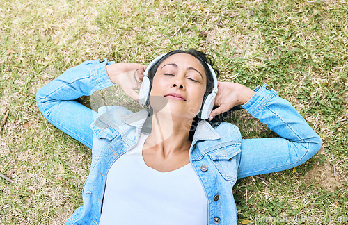 Image of Music, headphones and woman relax in a park, peace and zen from above, content and calm. Podcast, earphones and girl resting while listening to audio for wellness, stress free and chilling on grass