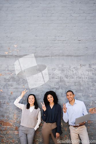 Image of Business people, peace sign and portrait of friends by a brick wall with a laptop and digital tablet. Happy, smile and corporate team employees standing together with a hand gesture in the urban city