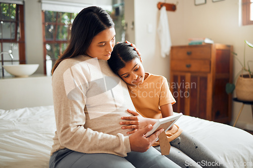 Image of Pregnant mom and child look at a picture frame together in the bedroom of their modern house. Sad, emotional and mother with pregnancy holding her girl kid while looking at a photo on the bed at home