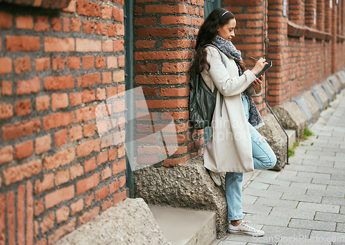 Image of Woman, student and tablet relaxing on brick wall writing, design or doing research in the city. Female university learner working on touchscreen with wireless pen or tech in a urban town