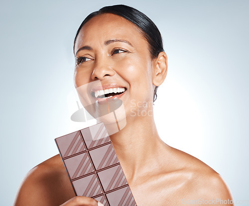 Image of Chocolate, smile and senior woman thinking of health isolated on a blue background in studio. Food, happy and face of an elderly model with an idea for candy, sugar snack and sweets on a backdrop