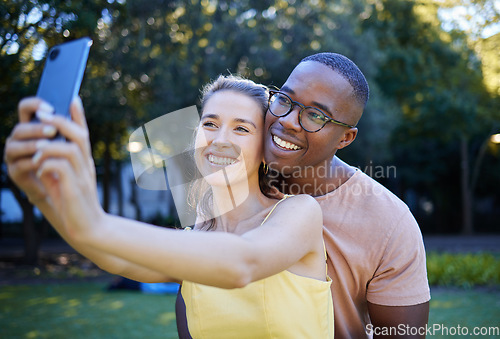 Image of Selfie, phone and interracial couple smile in park enjoying weekend, summer holiday and quality time together. Nature, dating and happy man and woman relax, calm and hug to take picture on smartphone