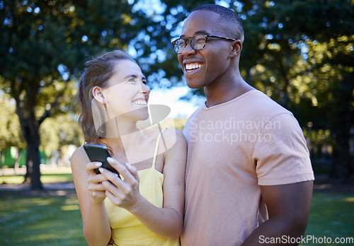 Image of Comedy, laughing and interracial couple with a phone in nature, funny communication and smile at a meme. Comic, streaming and black man and woman reading a joke on a mobile in a park in France