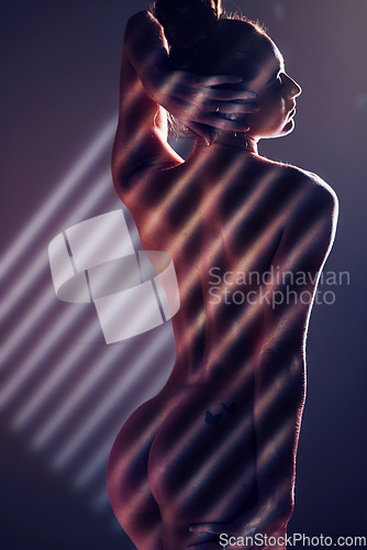 Image of Sensual, blinds and woman posing in a studio with an alluring, sexy and seductive pose with light. Slim, naked and nude body of a female model with stripe pattern isolated by a dark black background.