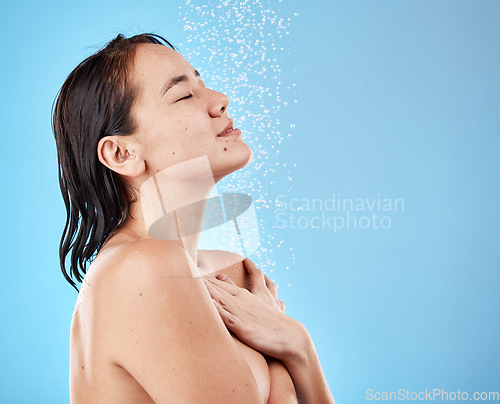 Image of Asian woman in shower, water on face and skincare beauty with healthy wet hair on blue background. Wellness in studio, washing natural body care in bathroom or hygiene cleaning stream of water drops
