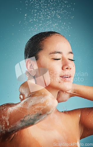 Image of Shower, water and hygiene with a woman cleaning in studio on a blue background for wellness and fresh. Bathroom, relax and wet with an attractive young female washing her face or body for hydration