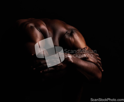 Image of Art, masculinity and artistic shadows with african man posing naked in studio isolated against a dark background. Muscular, macho and artwork of a strong black man curled up with hands over his head