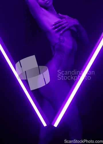 Image of Nude, desirable and alluring woman posing naked in a studio. Beautiful, sensual and young woman behind purple lighting in a v shape. A female feeling sexy and covering her breasts in a dark studio