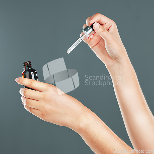 Image of Skincare, beauty and hands with face serum in a studio for a health, wellness and natural skin routine. Cosmetic, self care and facial oil for a healthy facial treatment isolated by a gray background