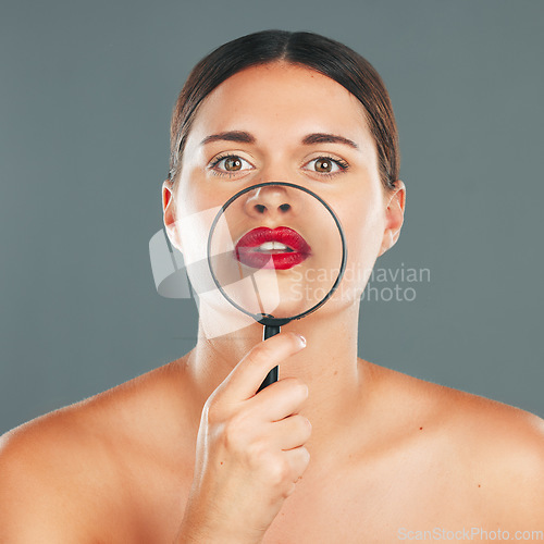 Image of Beauty, magnifying glass and portrait of a woman in studio with a makeup, skincare and natural routine. Face, cosmetic and female model with glass lens on her mouth while isolated by gray background.